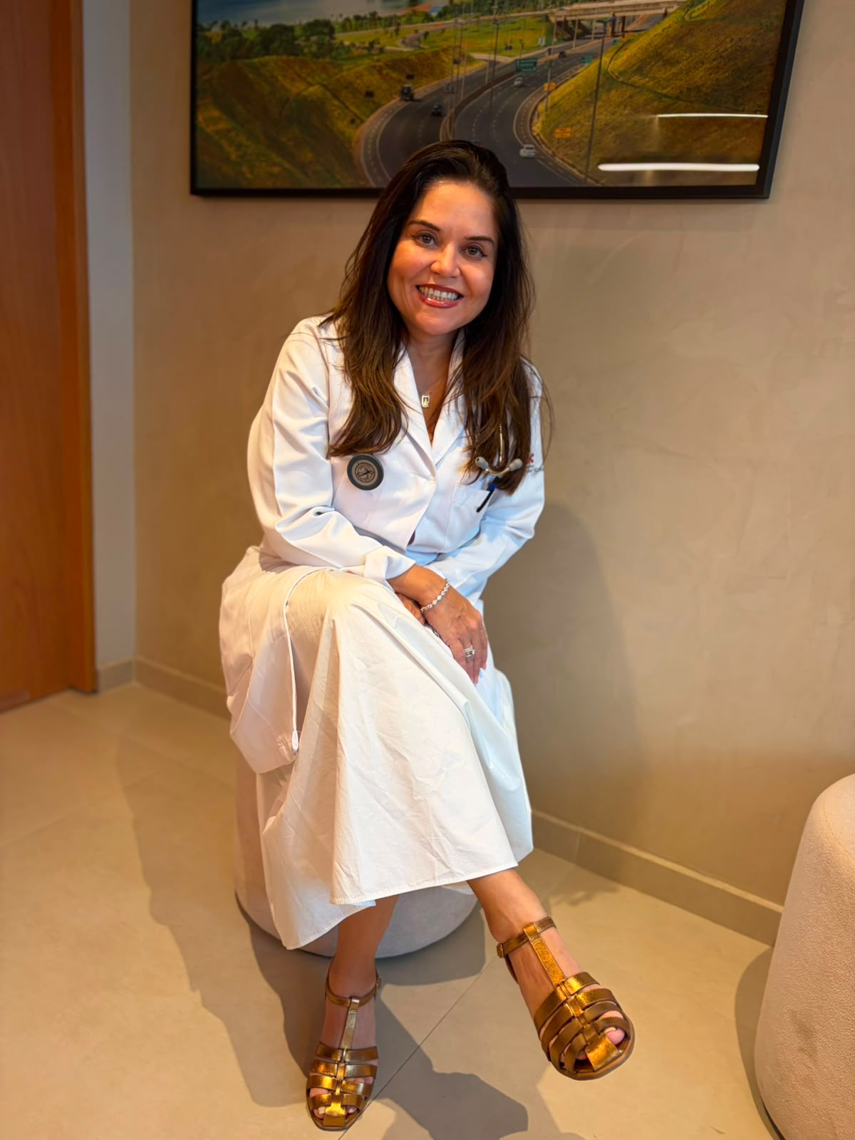 Dra. Hélia Beatriz sentada, sorrindo, em seu consultório