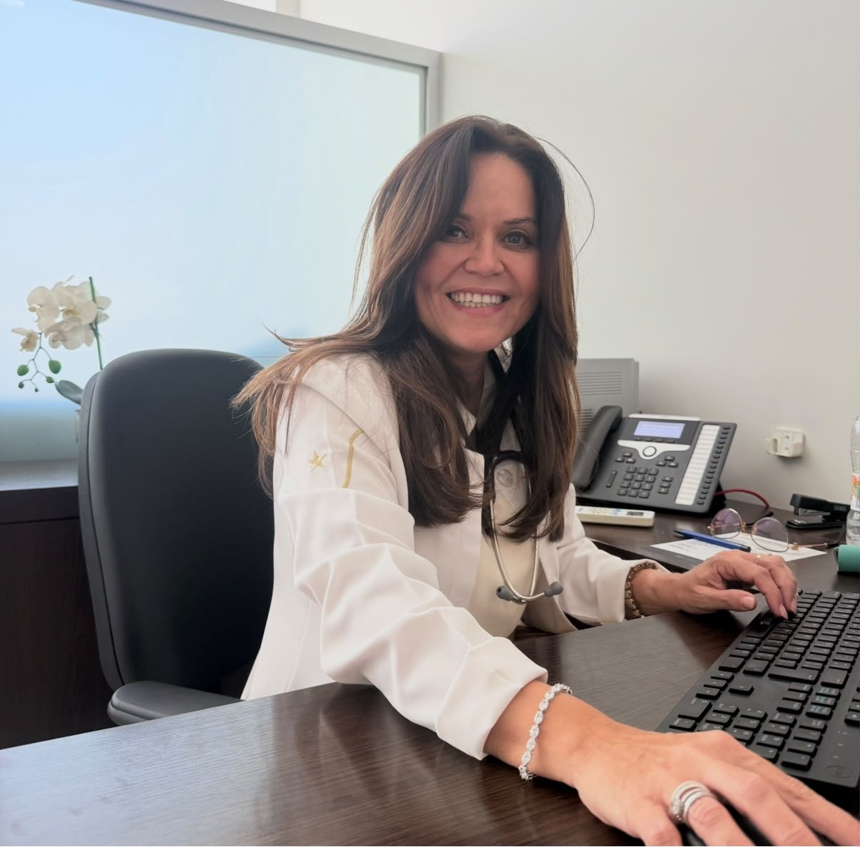 Dra. Hélia Beatriz sorrindo em sua mesa de atendimento