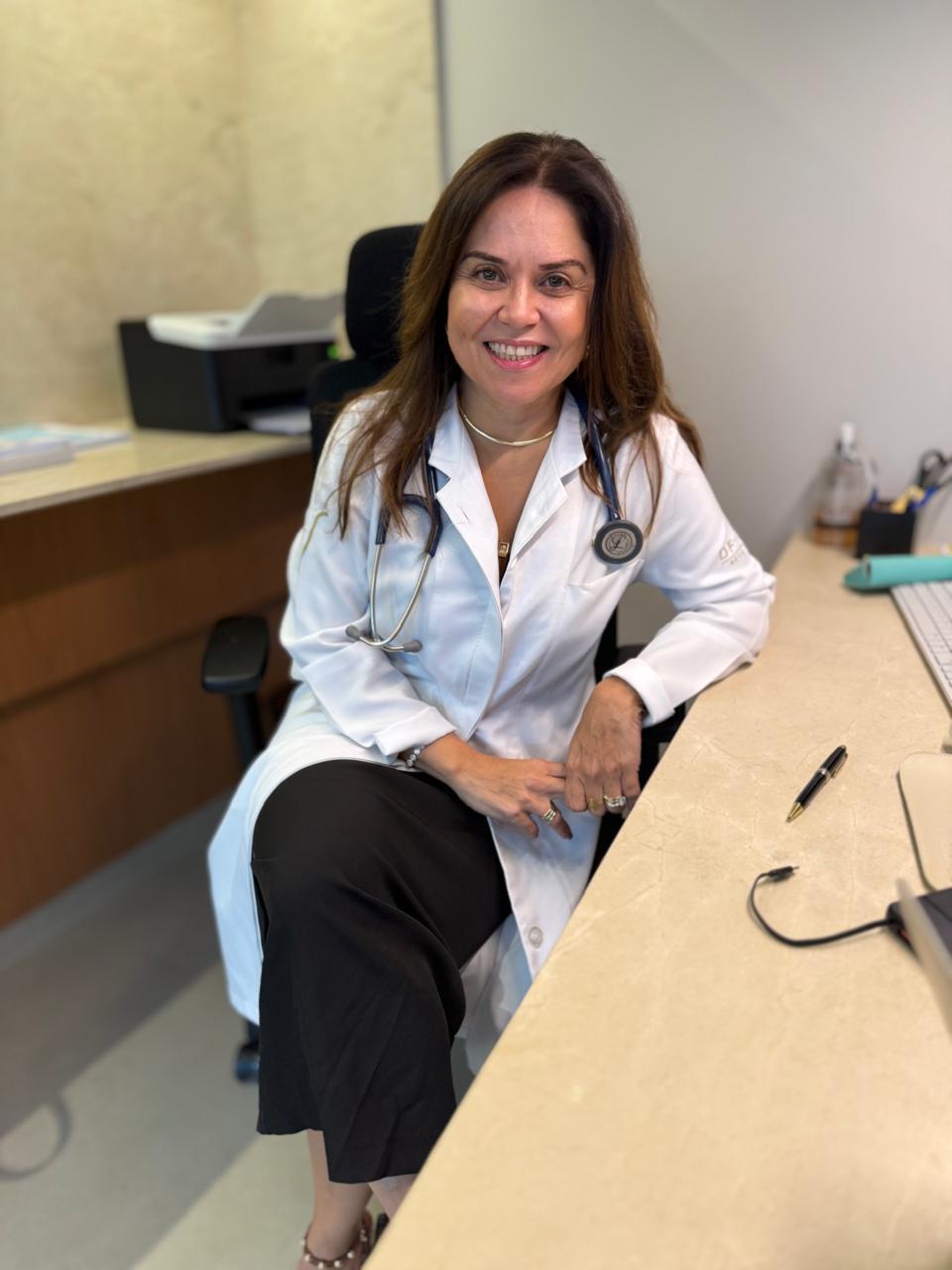 Dra. Hélia Beatriz sorrindo em sua mesa de atendimento